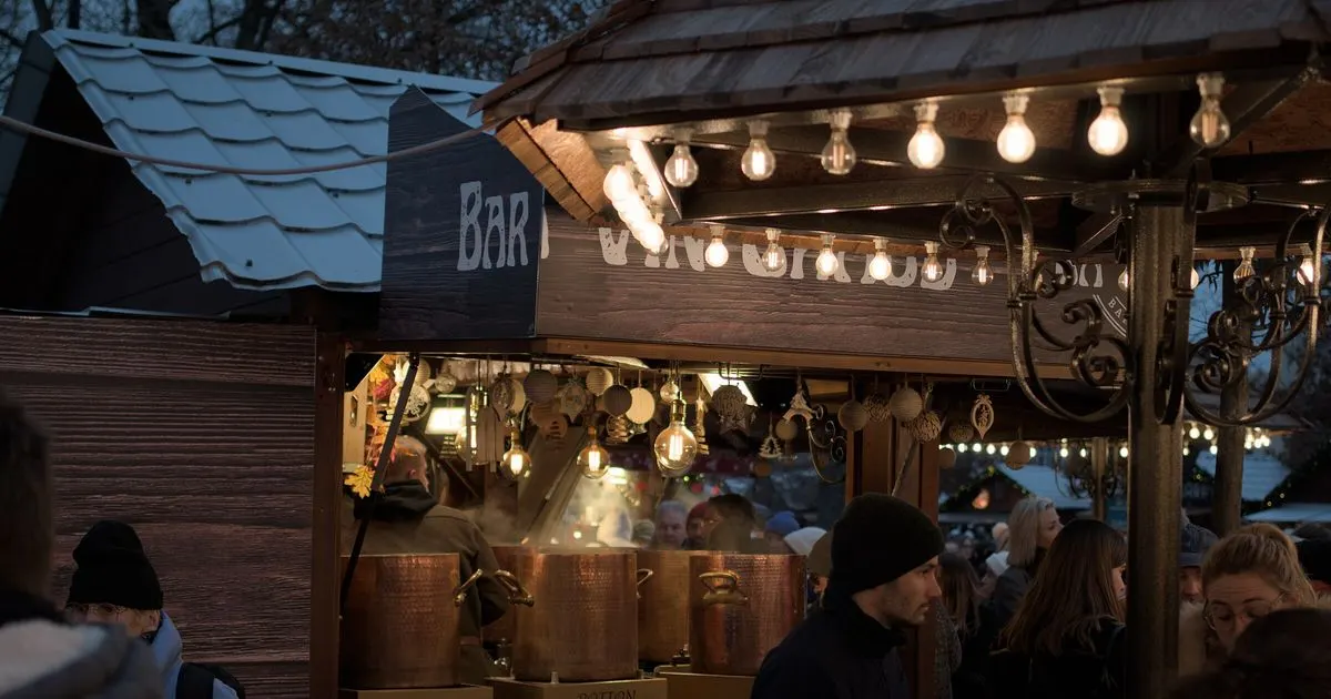 Stand de vin chaud éclairé à la tombée de la nuit sur un marché de Noël, avec ses marmites en cuivre et des passants emmitouflés