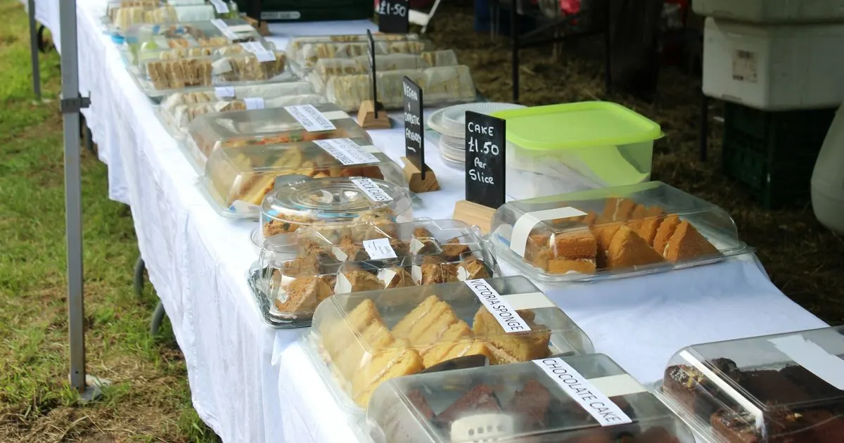 Table de gâteaux faits maison sous une tente, en plein air : parts de cake en boîtes, ardoises de prix à la part